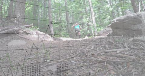Mid-adult female cyclist riding uphill on wooded trail with graph overlay and metrics