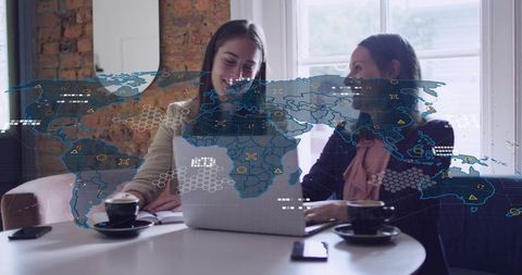 Two women collaborating over laptop at cafe with global data map and tech overlay