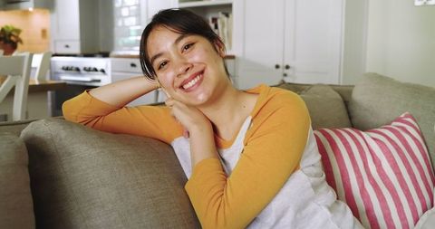 Smiling Asian Woman Relaxing on Sofa in Cozy Living Room