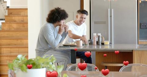Two young men sharing cozy morning breakfast at modern kitchen island with heart overlays
