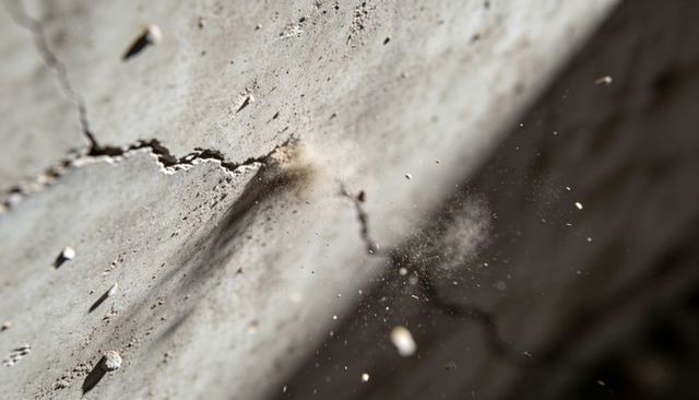Cracked concrete ejecting dust plume and flying debris in macro close-up studio texture