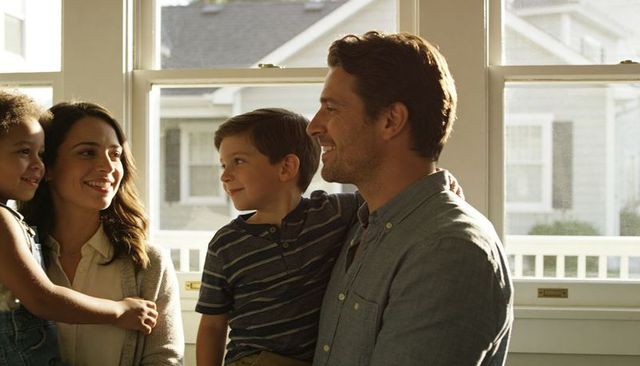 Sunlit family bonding holding children and smiling together in porch-facing window