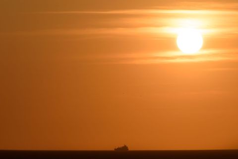 Cargo Ship Sailing Across Golden Sunset Horizon with Expansive Orange Sky