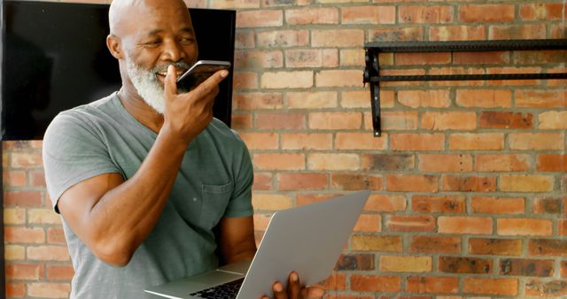 Senior Man Using Voice Command on Smartphone While Holding Laptop in Modern Loft - Download Free Stock Images Pikwizard.com