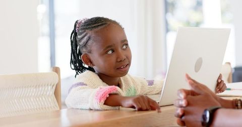 African American Girl Pointing at Laptop While Learning with Adult Guidance at Home