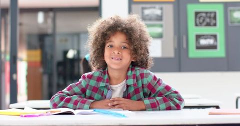 Smiling girl studying in classroom with open notebook and pencils