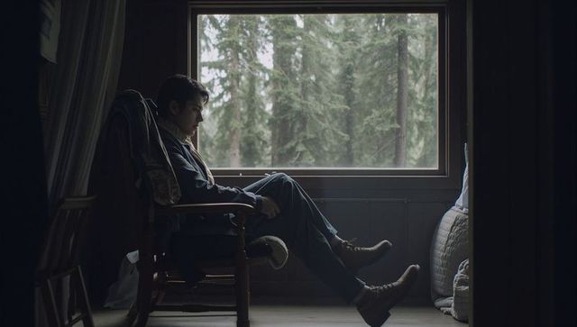 Man sitting in rocking chair gazing through cabin window with forest view