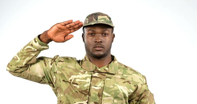 A young African American military man salutes in his camouflage uniform, with copy space. His expression is serious, reflecting the discipline and respect inherent in military service.