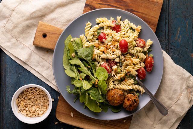 Fresh spiral pasta with cherry tomatoes and vegetables served with meatballs and a side salad on a plate. Ideal for use in food blogs, recipe websites, and culinary magazines. Perfect for promoting healthy eating, organic food, and homemade meals.