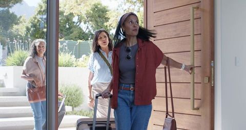 Mature women returning home pulling luggage through modern front door