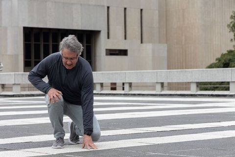 Mature man kneeling on zebra crosswalk preparing for stretching and urban fitness routine