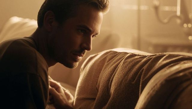 Warm golden-lit intimacy: man leaning, watching partner resting on knit-sweater sofa