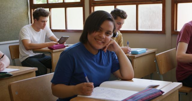 Young student smiling while studying in classroom with books and pen. Useful for educational materials, school promotions, and articles about academic environments, positive learning experiences, and youth education.