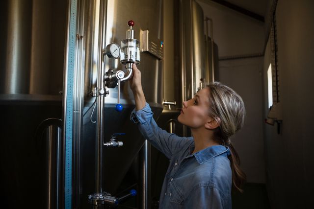 Female worker examining storage tank at brewery, focusing on quality control and brewing process. Ideal for use in articles about beer production, industrial work environments, and women in manufacturing.