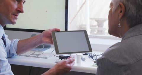 Doctor Consults Senior Patient Using Tablet Technology in Medical Office
