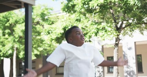 African american boy jumping with arms outstretched in sunlit courtyard on campus