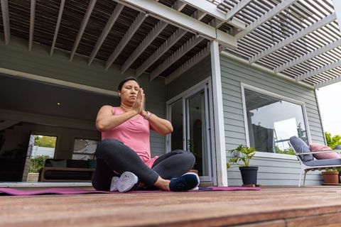 Woman practicing mindful meditation on wooden deck yoga mat under pergola