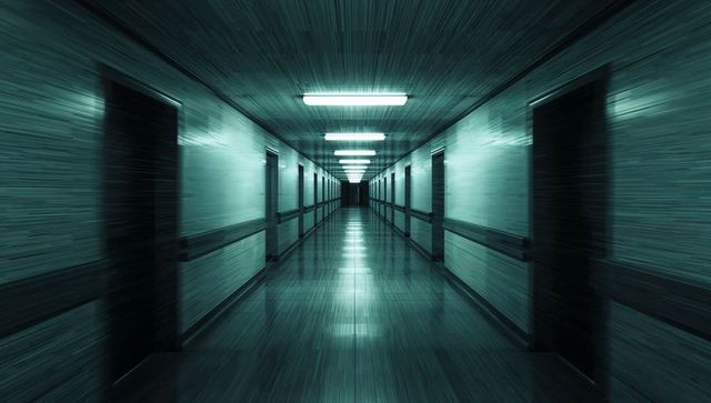 Empty teal hospital corridor leading to dramatic vanishing point with symmetry and glossy floor