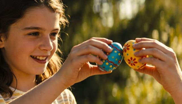 Smiling preteen girl tapping colorful painted eggs in sunny backyard easter moment
