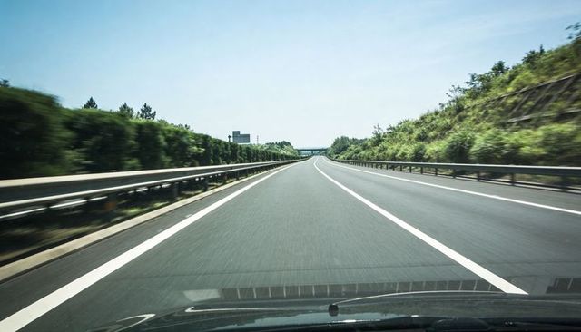Empty highway driving perspective from car hood on sunny day with overpass, guardrails
