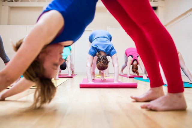 Trainer assisting group of people with downward dog pose yoga exercise in the fitness studio