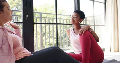 Women stretching together on mats near sliding door during home workout and wellness chat