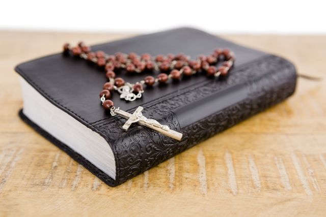This image shows a close-up of a Bible with rosary beads placed on a wooden table. The intricate design of the Bible cover and the detailed cross on the rosary beads highlight the importance of faith and devotion in Christianity. This image can be used in religious articles, church bulletins, spiritual blogs, or educational materials about Christianity and Catholic practices.