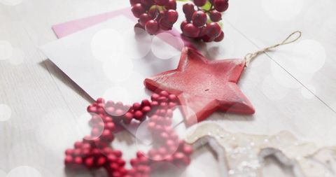 Red star ornament resting with beaded garland, berries and holiday envelope