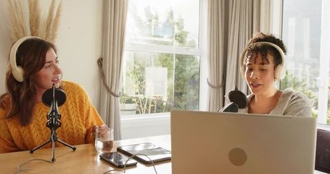 Recording podcast at home with diverse female co-hosts wearing headphones and using laptop