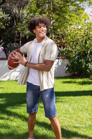 Young man tossing football in sunny suburban backyard, casual summer lifestyle