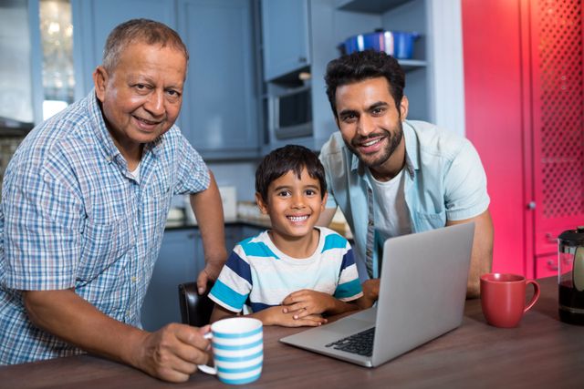 Smiling multi generation family using laptop at home. Grandfather, father, and son bonding in kitchen while using technology. Perfect for depicting family togetherness, generational bonding, and casual home activities. Useful for articles on family dynamics, technology use in families, and home life scenarios.