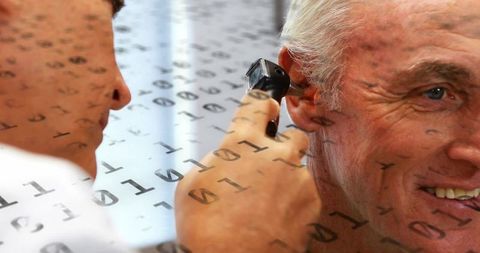 Clinician performing ear examination with otoscope on senior patient, digital data overlay
