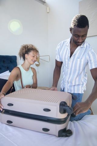 Diverse couple unpacking suitcase on bed preparing for travel getaway in modern bedroom