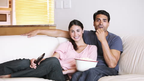 Happy Couple Relaxing on Couch with Popcorn and TV Remote