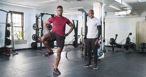 Trainer guiding client in resistance band balance exercise in modern gym