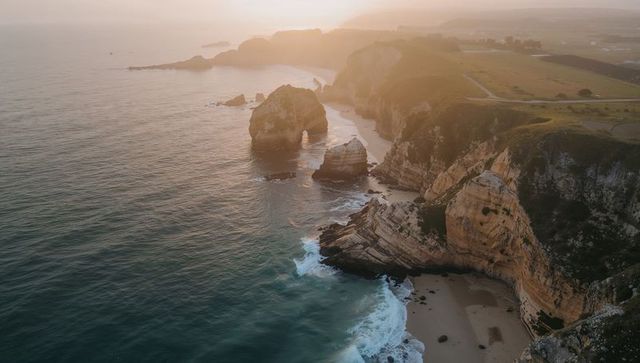 Golden hour coastal cliffs and sea stacks with natural arch overlooking farmland panorama