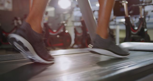 Focused on legs of person running on treadmill in gym, showcasing fitness commitment and health activities. Great for advertisements, fitness blogs, and health-related promotional material.