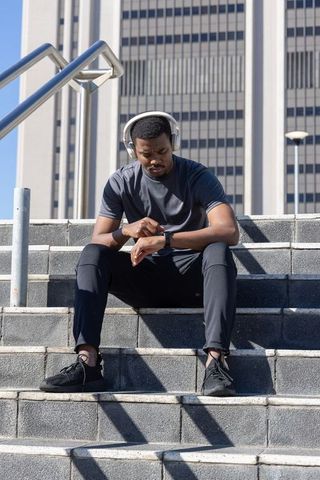 African american athlete checking smartwatch on urban steps wearing headphones