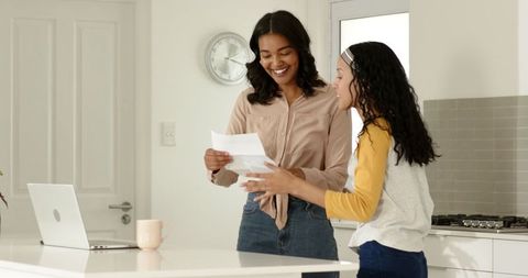 Smiling Mother and Daughter Reviewing Paperwork in Modern Kitchen