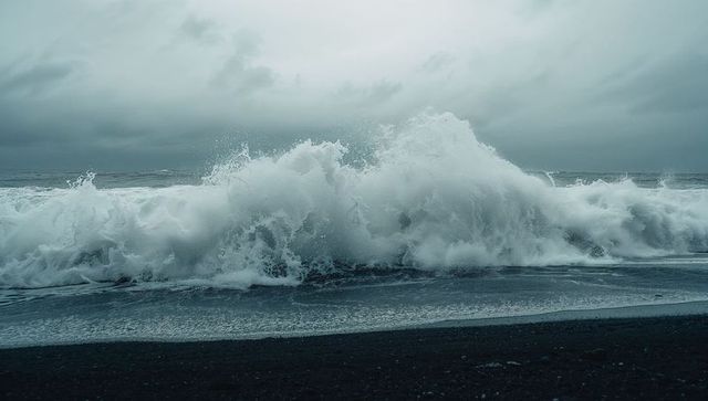 Crashing ocean wave against dark shoreline spraying foam under stormy overcast sky