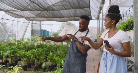 Coworkers Discussing Plant Care Techniques in Urban Greenhouse