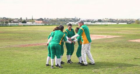 Diverse women's softball team celebrating in huddle on green field