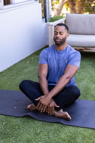 African american man practicing outdoor meditation and yoga on backyard mat for mindfulness
