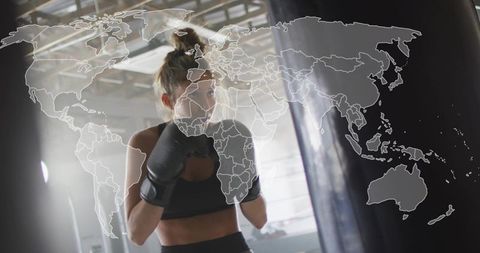 Female boxer training with heavy punching bag backlit gym world map overlay