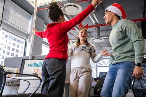 Diverse team celebrating holiday party in modern open-plan office wearing santa hat and antlers