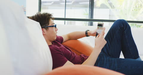 Teenage Boy with Glasses Using Tablet on Couch at Home