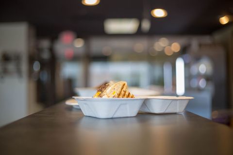 Grilled sandwich sitting in compostable clamshell on cafe counter with soft bokeh