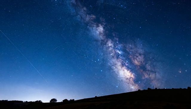 Milky Way Stretching Diagonally Over Rural Hillside at Night With Meteor Streak