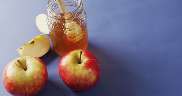Image of honey in jar, apples and apple slices lying on blue surface. food, cooking, baking, taste and flavour concept.
