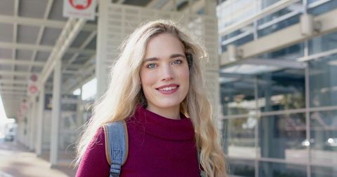 Smiling Young Woman with Backpack in Urban Transit Hub Wearing Maroon Turtleneck Portrait